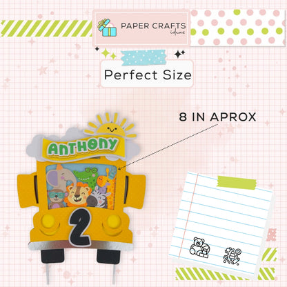 Yellow bus-shaped birthday cake topper with 'Anthony' and number '2', on a checkered background with stationery items.