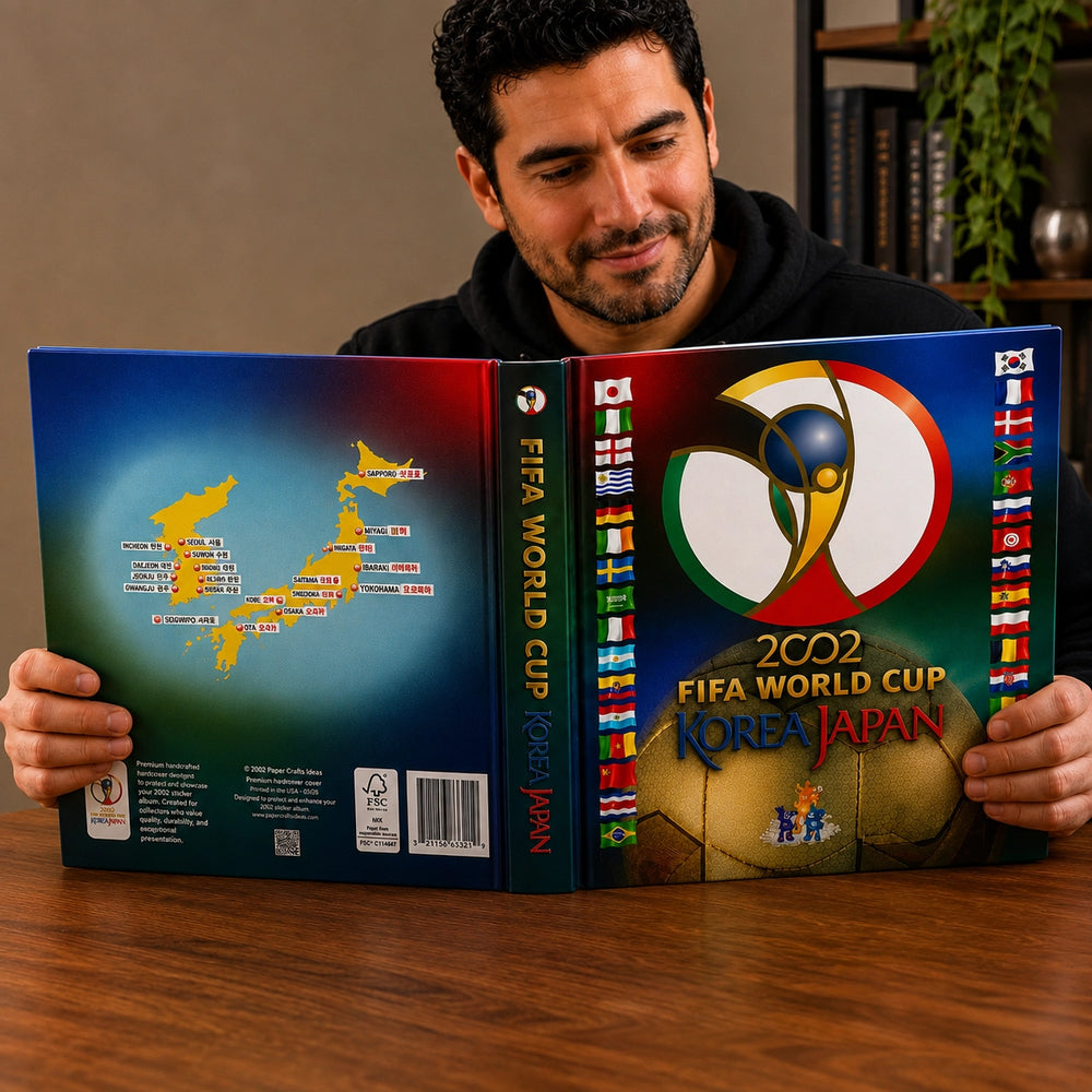 A man holds open a custom-designed hardcover book or album celebrating the 2002 FIFA World Cup in Korea and Japan, showing the front cover with the tournament logo and a soccer ball, the spine, and the back cover with a map of Japan.
