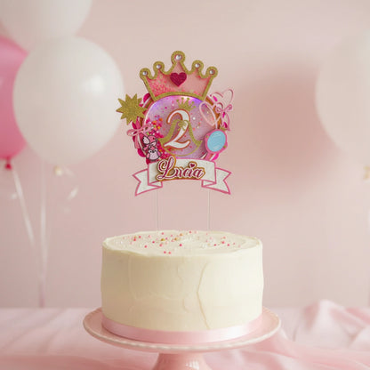 White cake with a decorative topper featuring a number '2' and the name 'Lina' on a pink background with balloons.