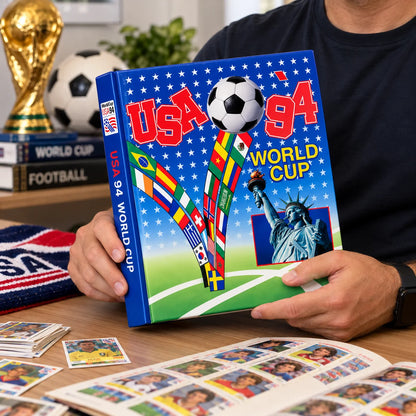 A person holds a hardcover book titled 'USA 94 World Cup' with a colorful cover featuring soccer imagery, flags, and the Statue of Liberty. The scene is set on a wooden table with soccer memorabilia, including a gold FIFA trophy replica, a soccer ball, and card decks, in the background.